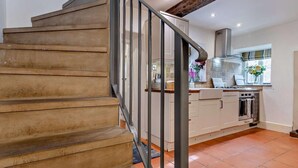 Eine Treppe führt zu einer Küche mit Fliesenboden, einem Fenster mit Blumen und einem modernen Herd.