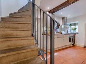 A staircase leading to a kitchen with a tiled floor, a window with flowers, and a modern stove. - 1 Bed in Matlock (oc-75400) (Middleton)