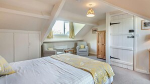 Ein Schlafzimmer mit einem Bett, zwei Stühlen, einem Holzschrank und einem Fenster mit Vorhängen.