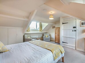 Ein Schlafzimmer mit einem Bett, zwei Stühlen, einem Holzschrank und einem Fenster mit Vorhängen.