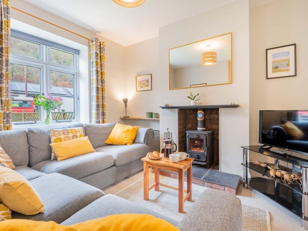 A living room with a sofa, a coffee table, a fireplace, a television, and a large window.