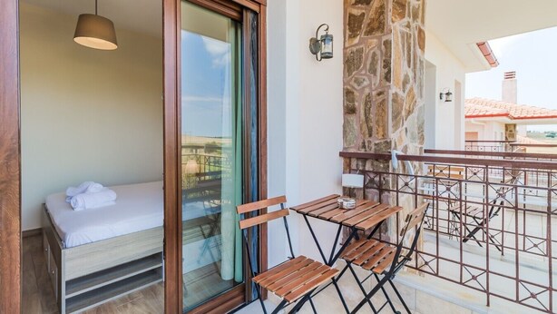 Un balcone con un letto, un tavolo, sedie e un muro in pietra.