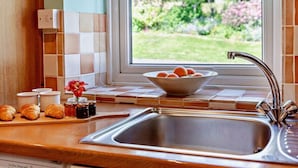 A kitchen with a stainless steel sink, a bowl of oranges, and a window with a garden view. - 2 Bed in Keswick (oc-sz145) (Braithwaite)