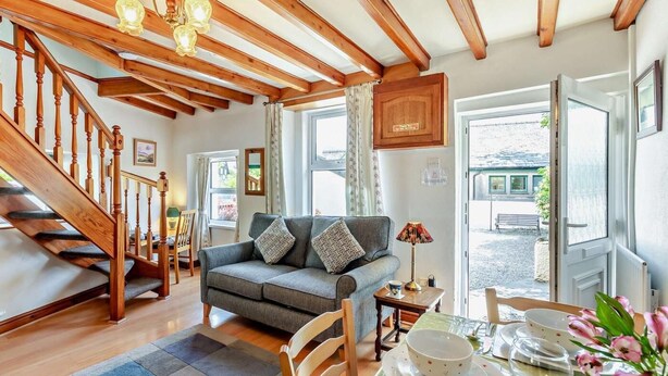 A cozy living room with a sofa, a dining table set with plates and a wine glass, a staircase, and wooden beams on the ceiling. - 2 Bed in Keswick (oc-sz145) (Braithwaite)
