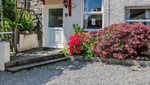 A stone building with a white door, a small porch, and a window. - 2 Bed in Keswick (oc-sz145) (Braithwaite)