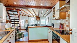 A modern kitchen with wooden beams, a central island, and a dining area with a sofa and table. - 2 Bed in Keswick (oc-sz145) (Braithwaite)