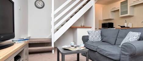 A modern living room with a grey sofa, a small black coffee table, a TV on a wooden stand, and a staircase with white railings.