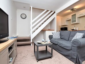 A modern living room with a grey sofa, a small black coffee table, a TV on a wooden stand, and a staircase with white railings. - 1 Bed in Redcar (oc-75726) (Marske-by-the-Sea)