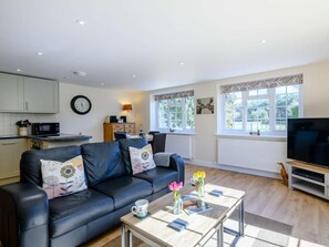 Ein Wohnzimmer mit einer schwarzen Ledersofa, einem Couchtisch mit Zeitschriften und Blumen, einem Fernseher und einer Küchenzeile mit Schränken und einer Mikrowelle.
