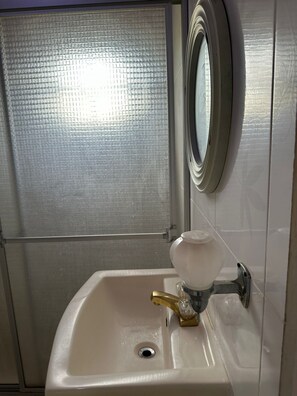 Baño con lavamanos blanco, grifo dorado, espejo y puerta de vidrio satinado.