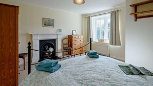Um quarto com lareira, uma cama com colcha floral, cômoda de madeira e uma janela com cortinas.