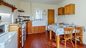Uma cozinha compacta com mesa de jantar, armários de madeira, forno embutido e piso ladrilhado.