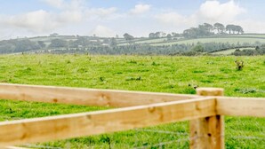 Paesaggio rurale con una recinzione di legno in primo piano e dolci colline sullo sfondo.
