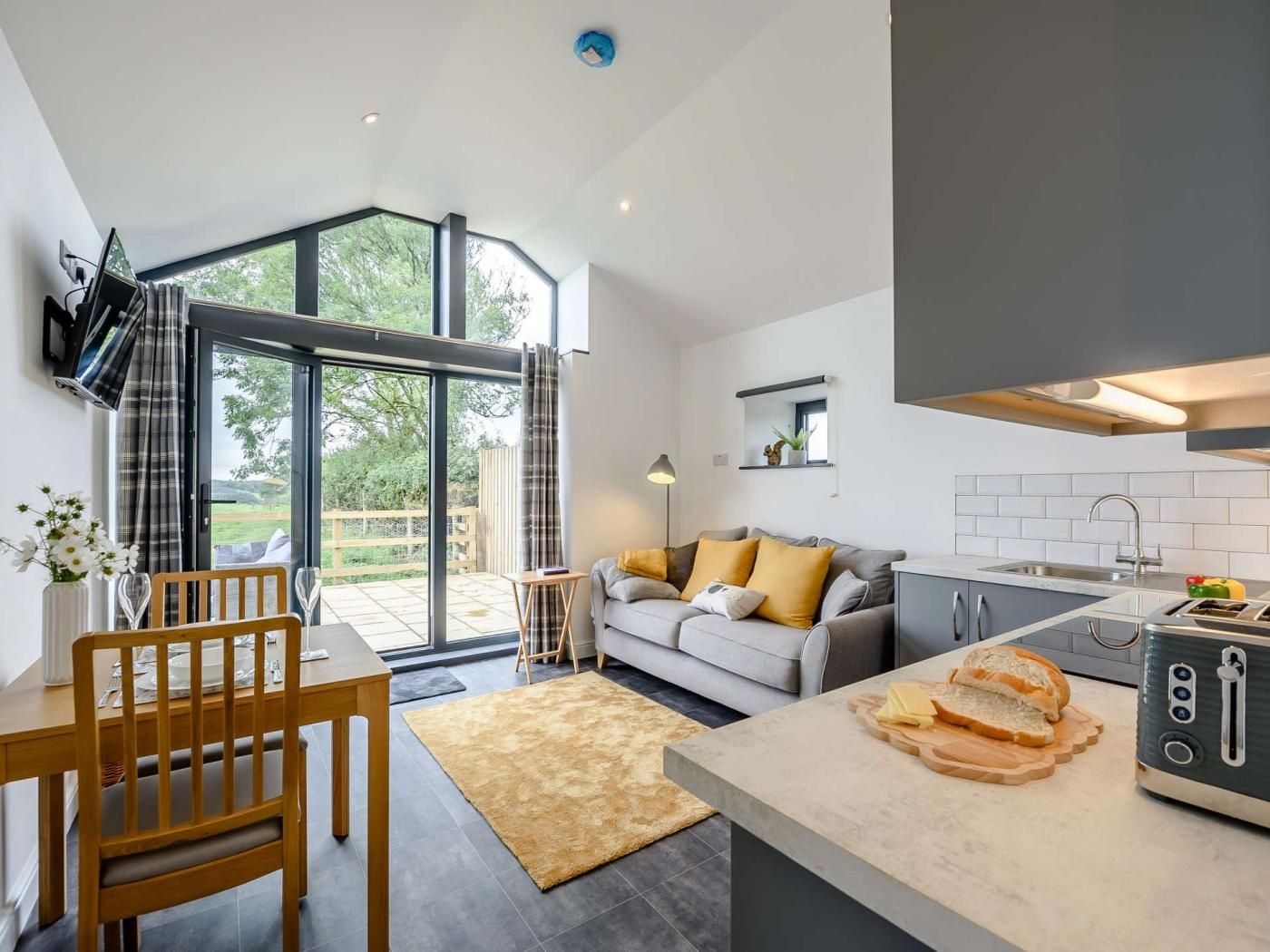 A modern kitchen with a built-in oven, a dining area with a wooden table and chairs, and a sofa with cushions.