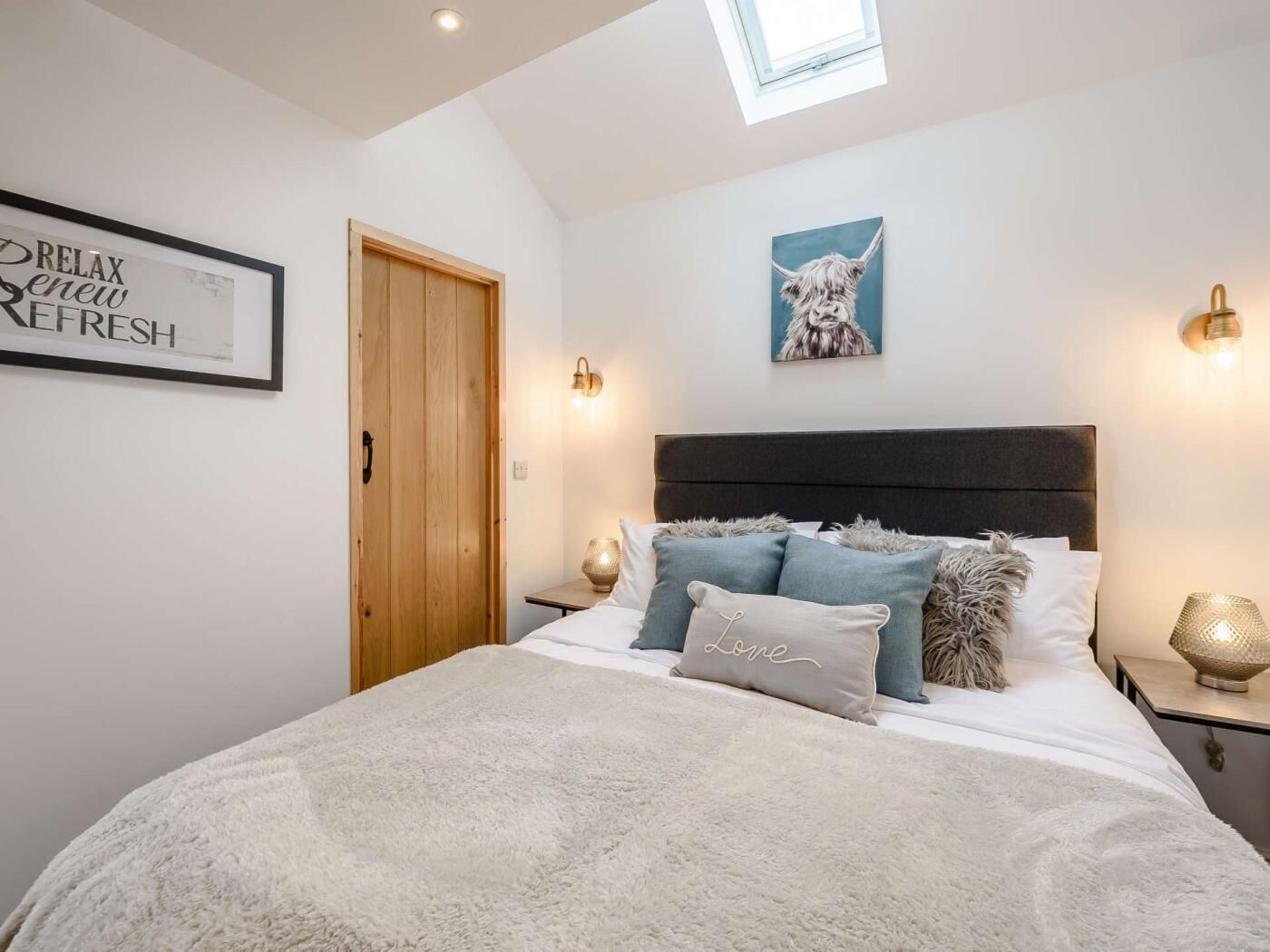 Une chambre à coucher avec un lit, une porte en bois, un panneau décoratif encadré, une lampe fixée au mur et un tableau.