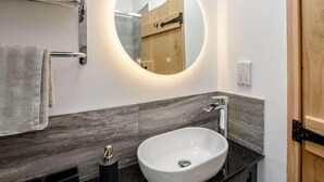 Un bagno con uno specchio rotondo, un lavandino bianco e un portasciugamani.
