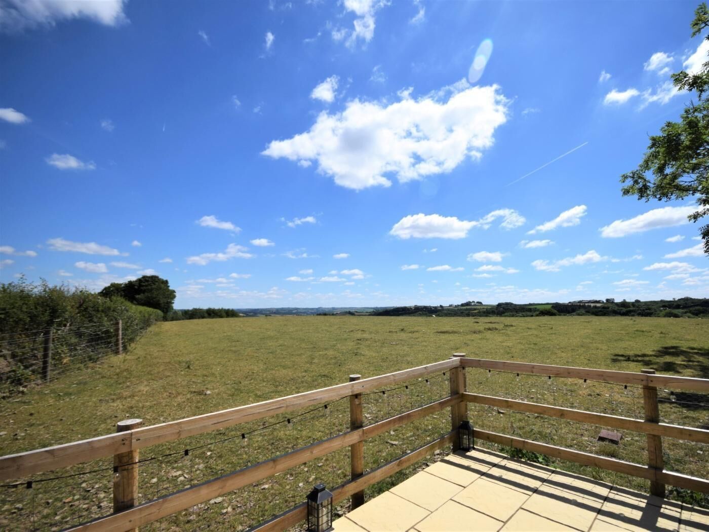 Une terrasse en bois offrant une vue sur un champ verdoyant et un ciel bleu dégagé.