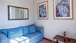 Um quarto com um sofá azul, um espelho e duas pinturas emolduradas na parede.