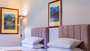 Quarto de hotel com duas camas, cada uma com roupa de cama e almofadas listradas, uma mesa de cabeceira, um abajur e quadros nas paredes.