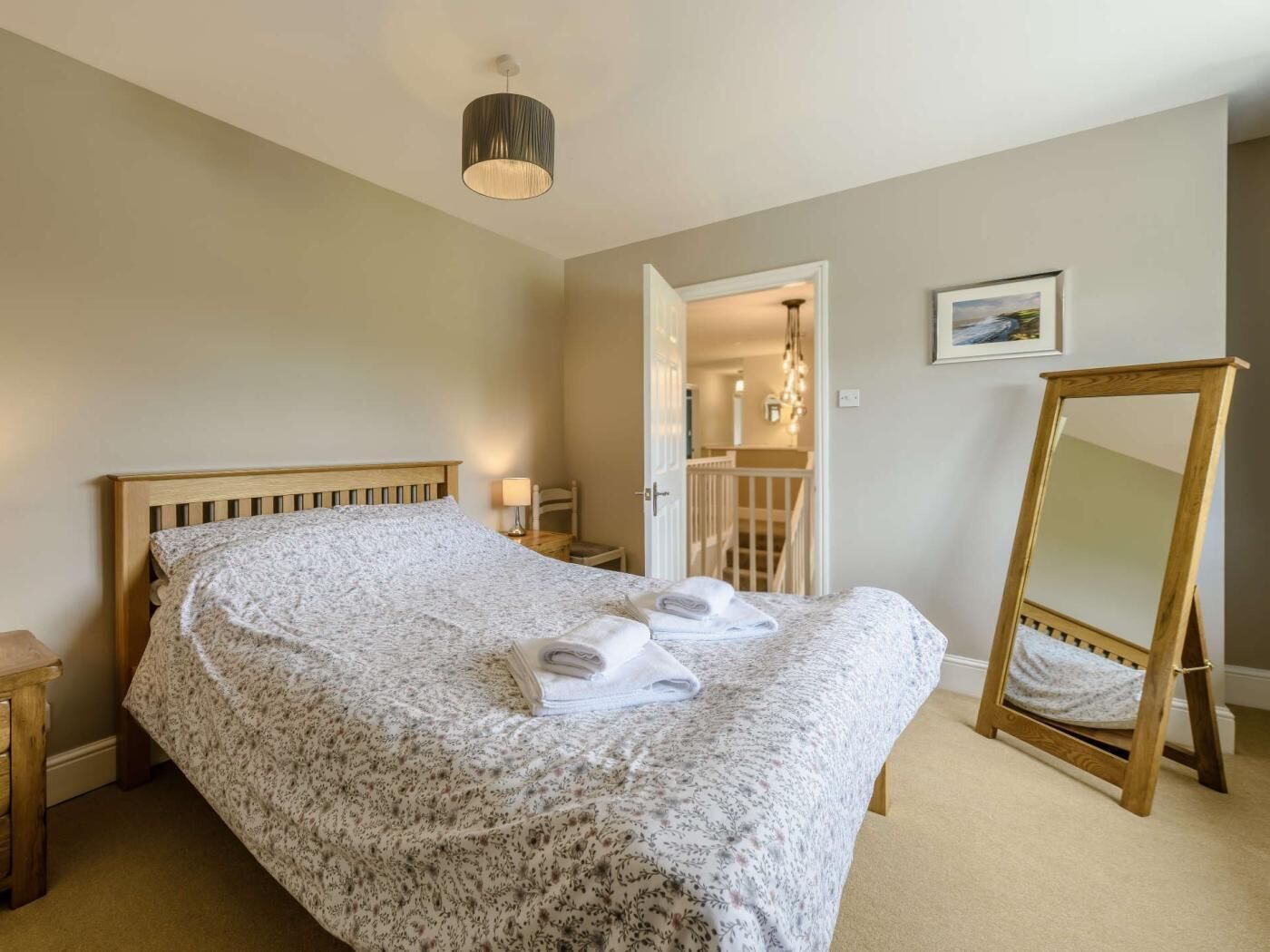 A bedroom with a wooden bed, a bedside table, a mirror, and a door leading to a staircase.