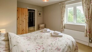A bedroom with a bed, a window with curtains, a radiator, and a wooden door. - 7 Bed in Bideford (oc-85428) (Woolfardisworthy)