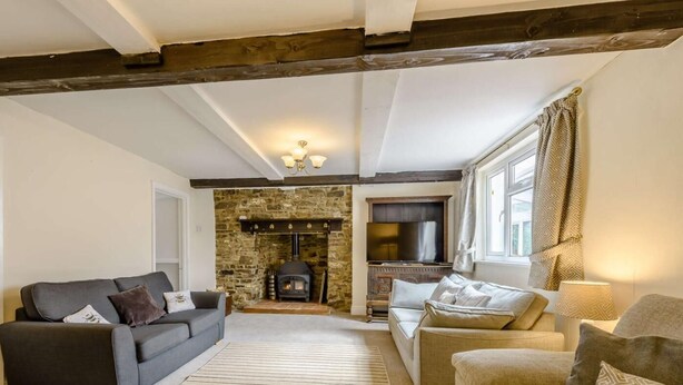 A cozy living room with a stone fireplace, two sofas, a TV, and a large window with curtains. - 7 Bed in Bideford (oc-85428) (Woolfardisworthy)