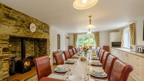 A dining room with a stone fireplace, a long table set for six, and a view of the outdoors. - 7 Bed in Bideford (oc-85428) (Woolfardisworthy)