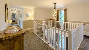 A hallway with a wooden desk, a white railing, and a staircase leading to a balcony. - 7 Bed in Bideford (oc-85428) (Woolfardisworthy)
