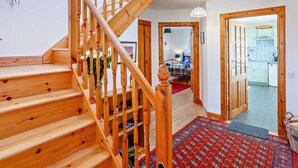 A wooden staircase leading to a bedroom with a bed, a red patterned rug, and a kitchen visible through an open door. - 3 Bed in Isle Of Skye (oc-ca071) (Aird of Sleat)