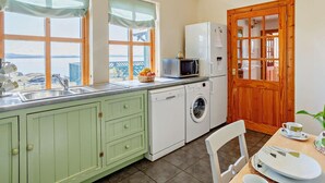 A kitchen with a view, a washing machine, a microwave, and a wooden door. - 3 Bed in Isle Of Skye (oc-ca071) (Aird of Sleat)