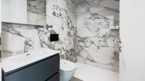 Et badeværelse med marmorvæg, vask, toilet og brusebad.