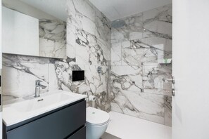 A bathroom with a marble wall, a sink, a toilet, and a shower. - {Suite 402} Gym, Business Room, Modern, Relax (Lugano)