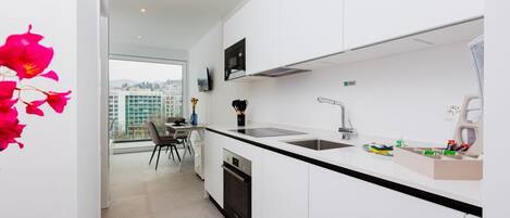A modern kitchen with white cabinets, a black countertop, a built-in oven, a sink, and a window offering a city view.