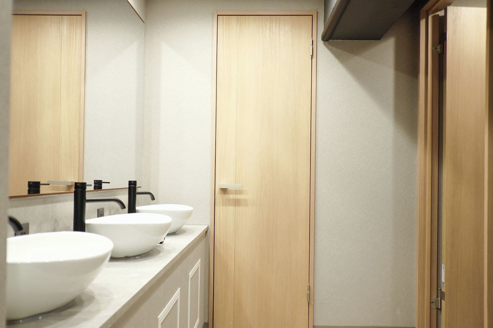 A bathroom with three white sinks, wooden doors, and a mirror.