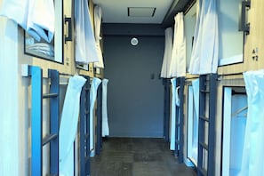 A corridor with bunk beds, each with a curtain and a small window. - LUMA URBAN HOTEL TAKADANOBABA (Tokyo)