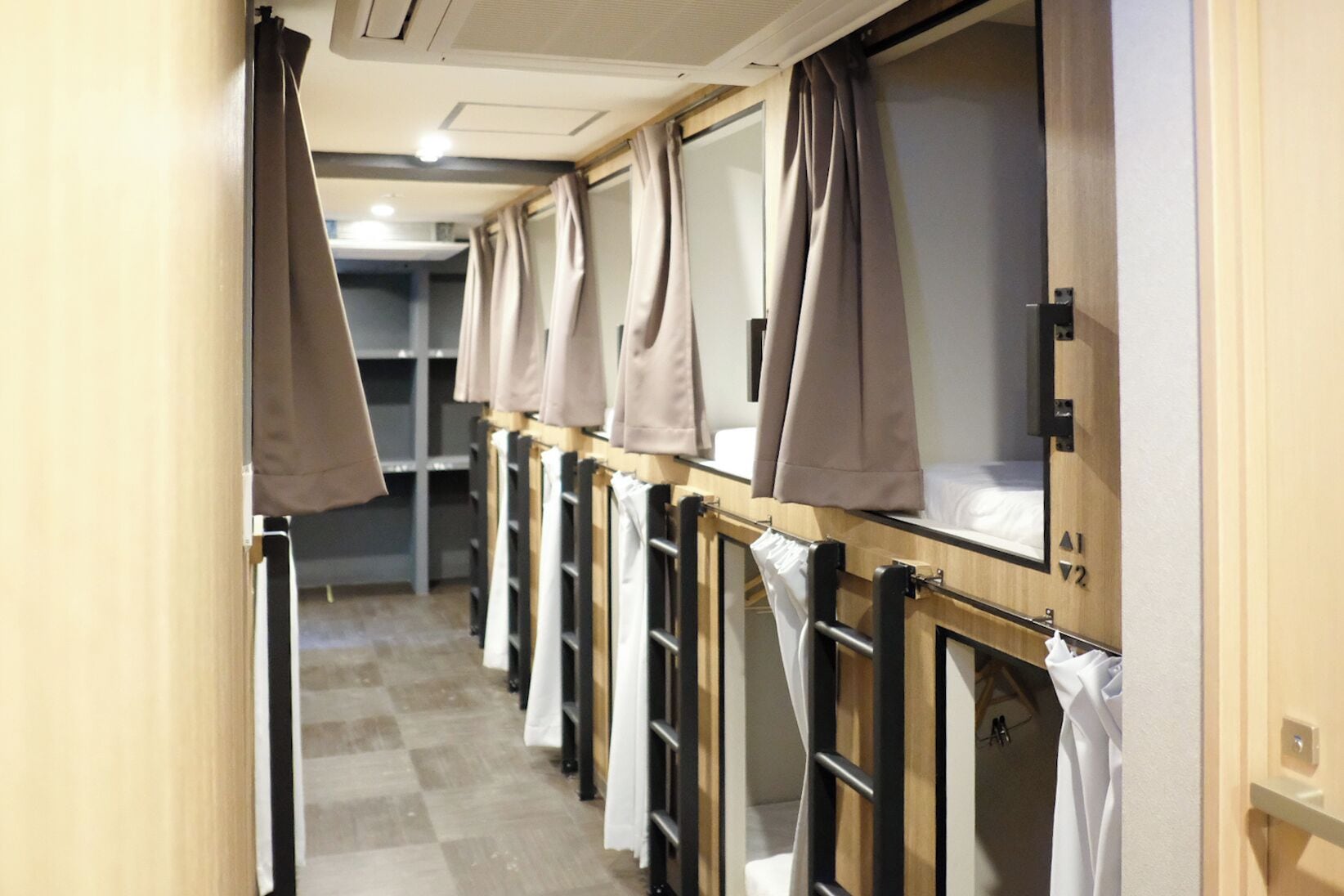 A corridor with bunk beds, each with a window and a curtain.
