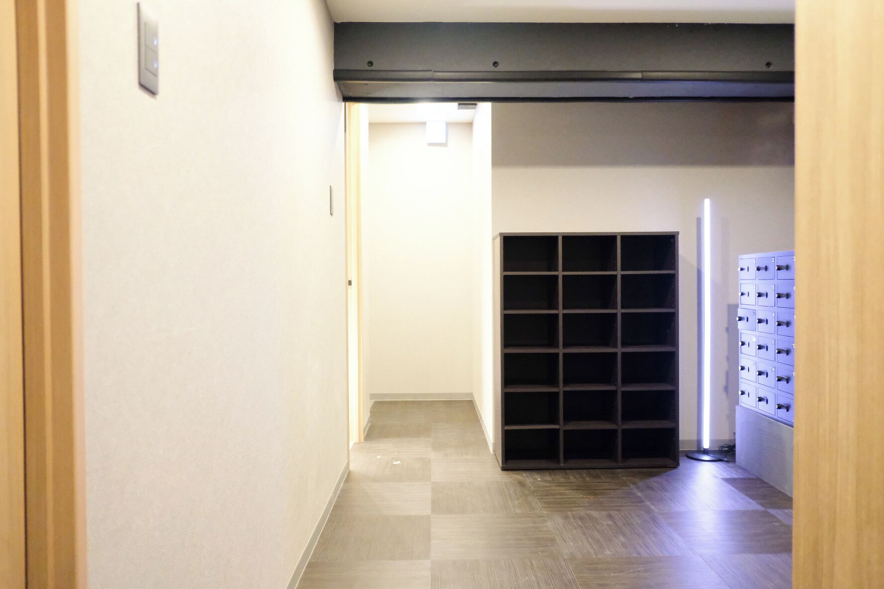 A hallway with a checkered floor, a door frame, a light switch, and a wall-mounted storage unit.