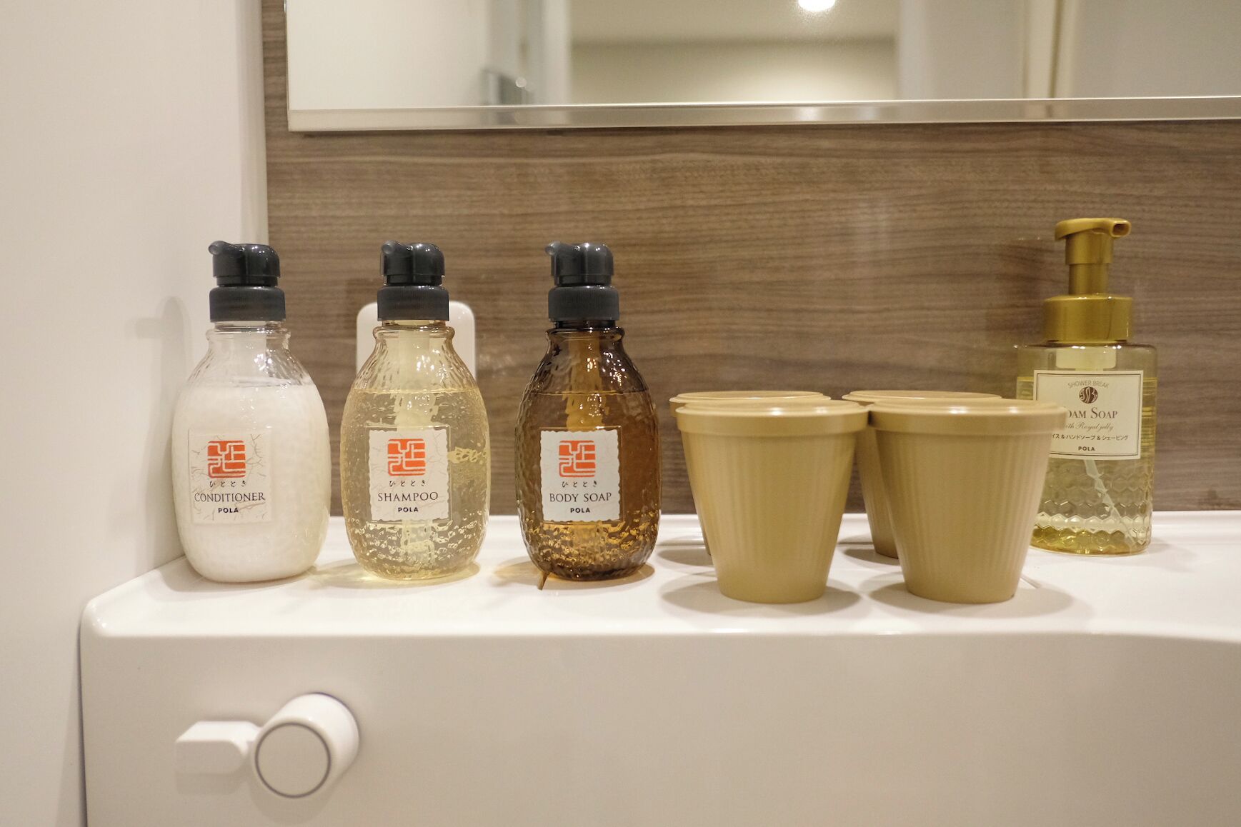 A bathroom counter with toiletries including a conditioner, shampoo, body soap, and a shower gel bottle.