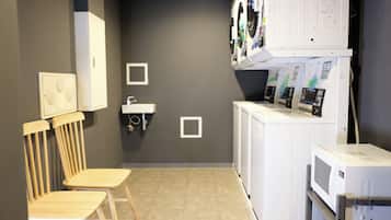 A laundry room with a sink, two wooden chairs, a washing machine, and a microwave.
