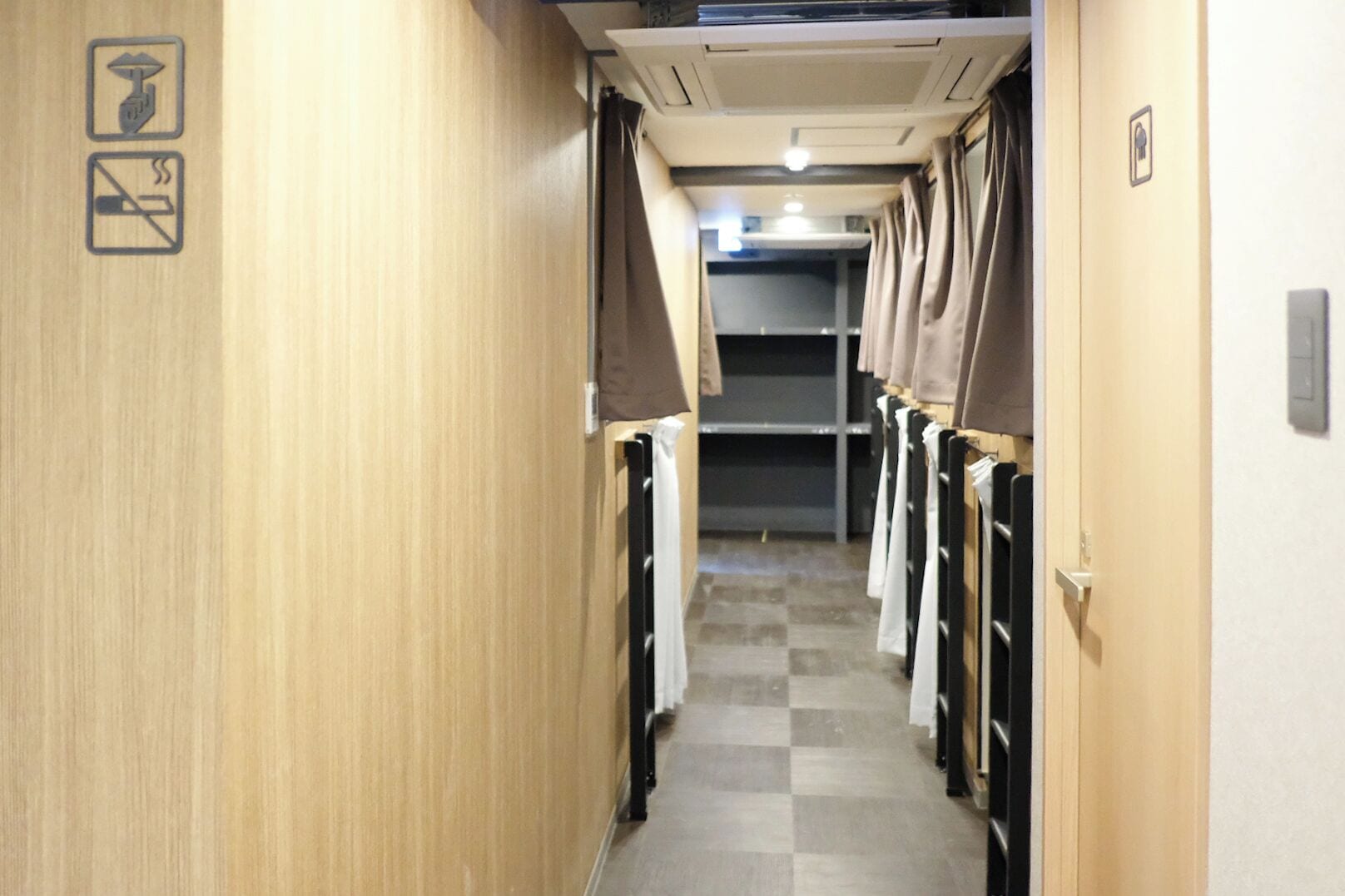 A narrow hallway with wooden walls, a checkered floor, and a row of black metal handrails on one side.