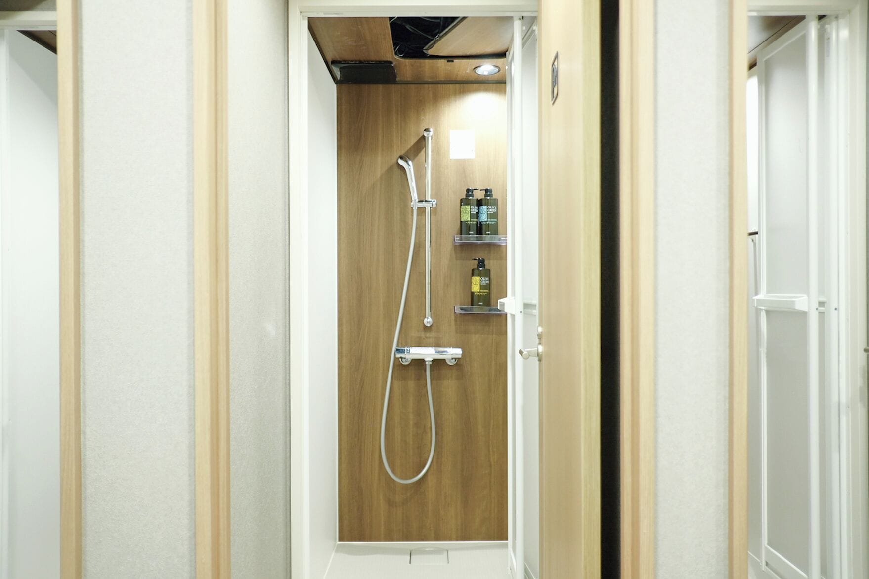 Une douche dotée d’une porte en bois, d’un pommeau de douche à main et d’une étagère pour les articles de toilette.