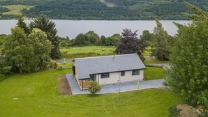 A house with a sloped roof, surrounded by a well-maintained lawn and a lake. - 3 Bed in Pitlochry (oc-ca207) (Tressait)