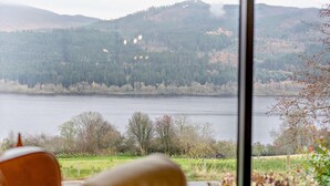 A room with a large window overlooking a lake and hills. - 3 Bed in Pitlochry (oc-ca207) (Tressait)