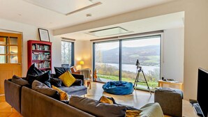 A modern living room with a large window, a red bookshelf, and a tripod with a camera. - 3 Bed in Pitlochry (oc-ca207) (Tressait)