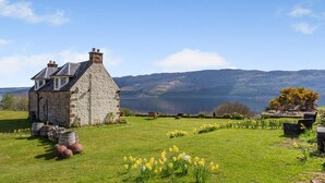 A stone house with a sloped roof, a grassy lawn, and daffodils in the foreground. - 2 Bed in Drumnadrochit (oc-ca315) (Strone)