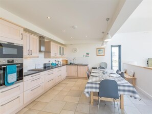 A modern kitchen with a dining area, featuring a large window, a built-in oven, and a dining table with chairs. - 4 Bed in Isle Of Skye (oc-ca326) (Uig)