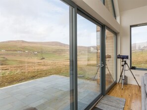 A room with large glass doors leading to a terrace, a telescope on a tripod, and a view of rolling hills. - 4 Bed in Isle Of Skye (oc-ca326) (Uig)