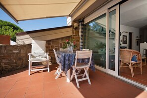 An outdoor patio with a table and two chairs, a potted plant, and a glass door leading to an interior space.