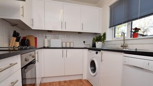 Uma cozinha moderna com armários brancos, máquina de lavar embutida e uma janela com persianas.