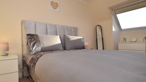 Quarto com cama, mesa de cabeceira, luminária, espelho e janela.